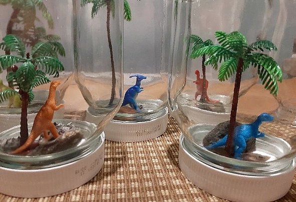 Miniaturdinosaurier und Plastikpalmen in umgedrehten Einmachgläsern als Schulprojekt