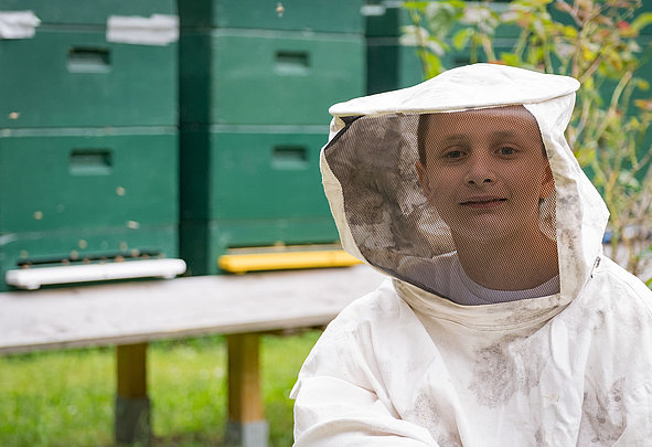 Kind im Imkeranzug vor grünen Bienenstöcken