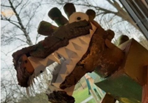Gebastelter Dinosaurierkopf aus Pappe mit gezackten Papierzähnen vor einem Fenster