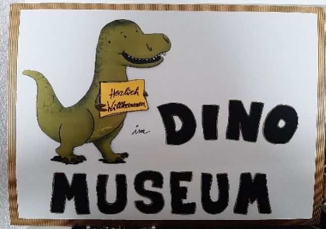Gezeichneter Dino hält Schild Herzlich Willkommen neben Schriftzug Dino Museum